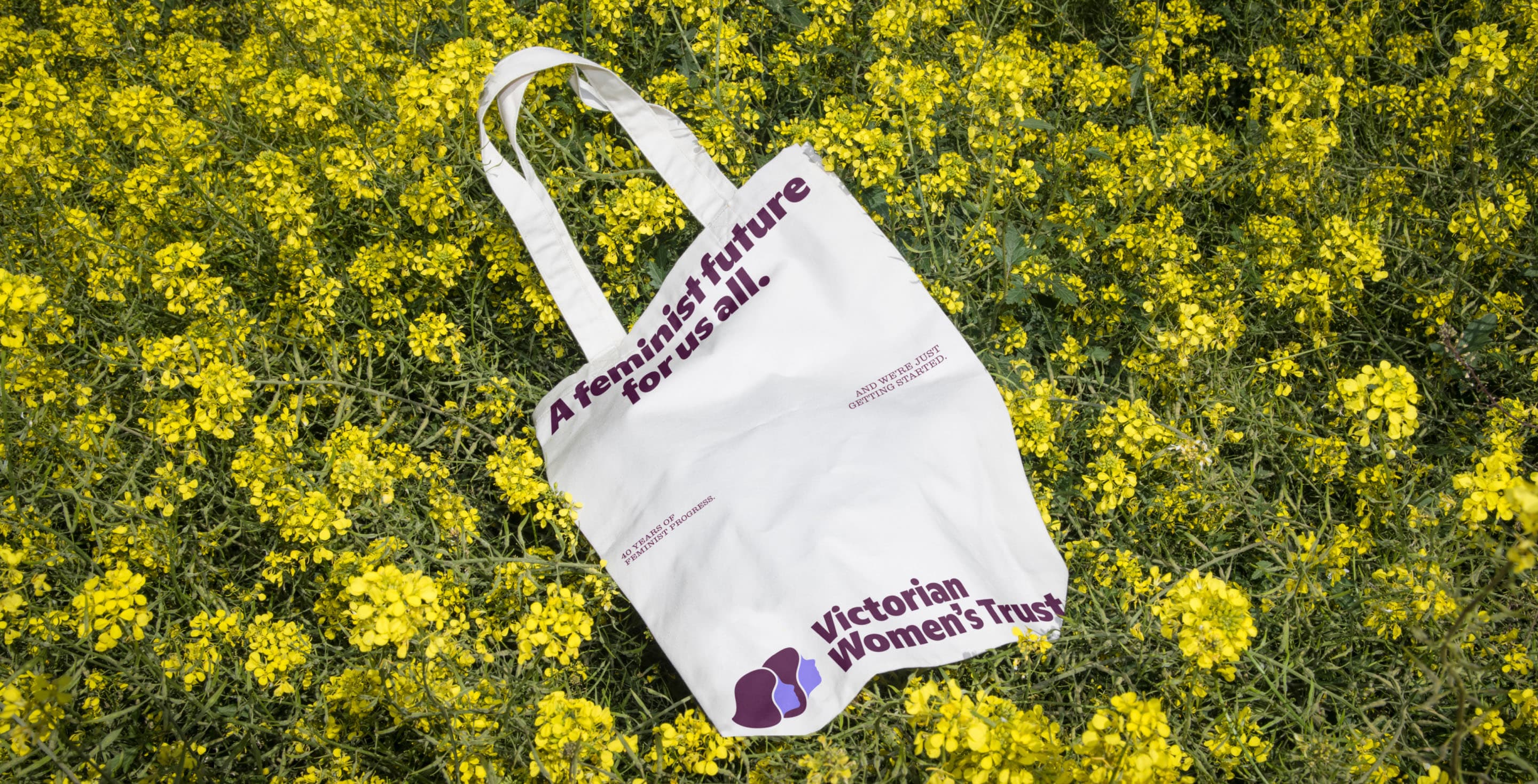 White Victorian Women’s Trust tote bag lying in a field of yellow wildflowers